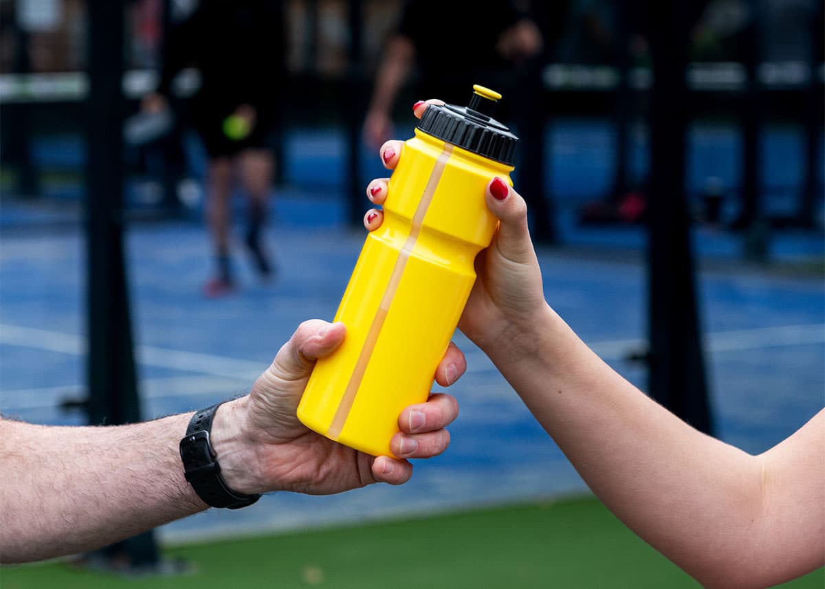 Gele bidon met twee handen die elkaar de bidon geven.