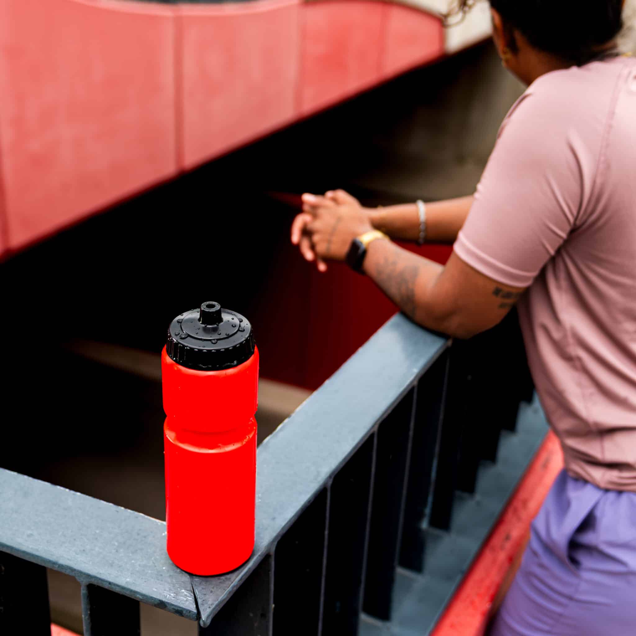Rode Eurobottle-bidon met zwarte valve cap op een reling naast een sporter.