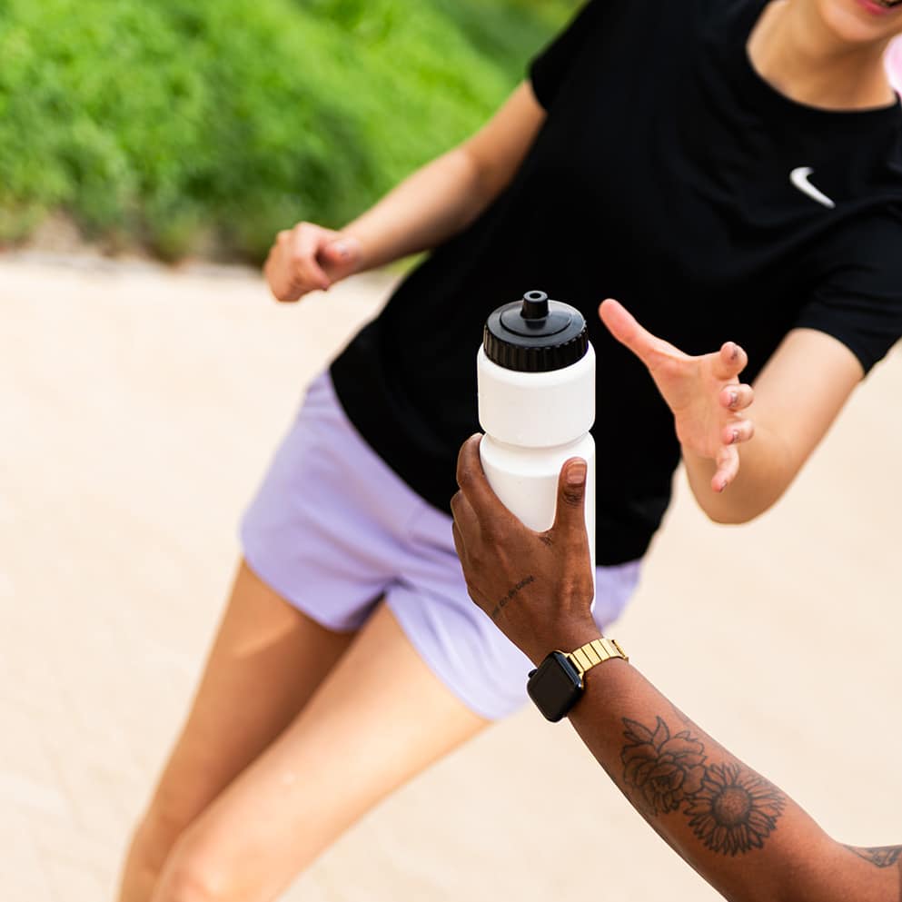 Witte Eurobottle-bidon met zwarte valve cap wordt doorgegeven aan een sporter.